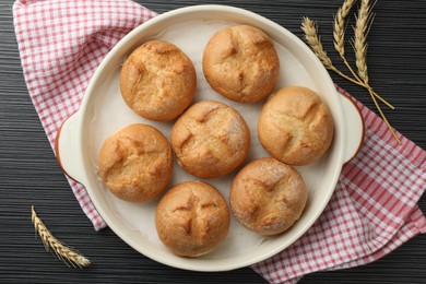 Baking dish with homemade tasty buns and spikelets on black wooden table, flat lay