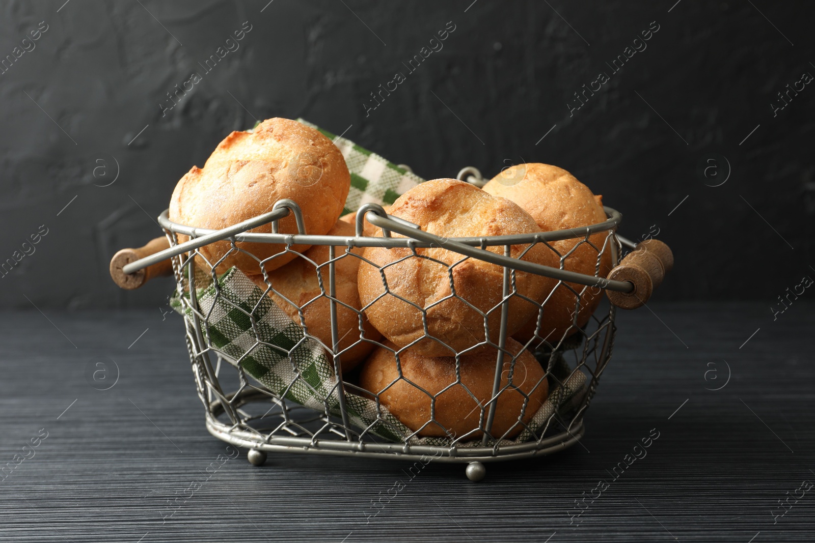 Photo of Metal basket with homemade tasty buns on black wooden table