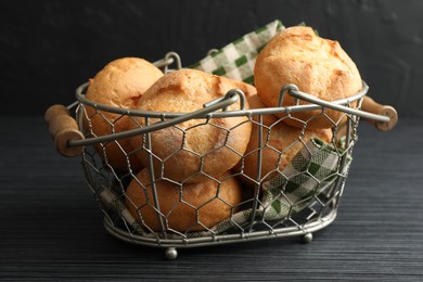 Photo of Metal basket with homemade tasty buns on black wooden table, closeup