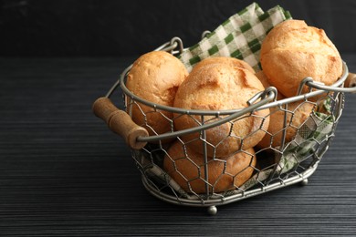 Photo of Metal basket with homemade tasty buns on black wooden table, closeup. Space for text