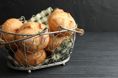 Photo of Metal basket with homemade tasty buns on black wooden table, closeup. Space for text