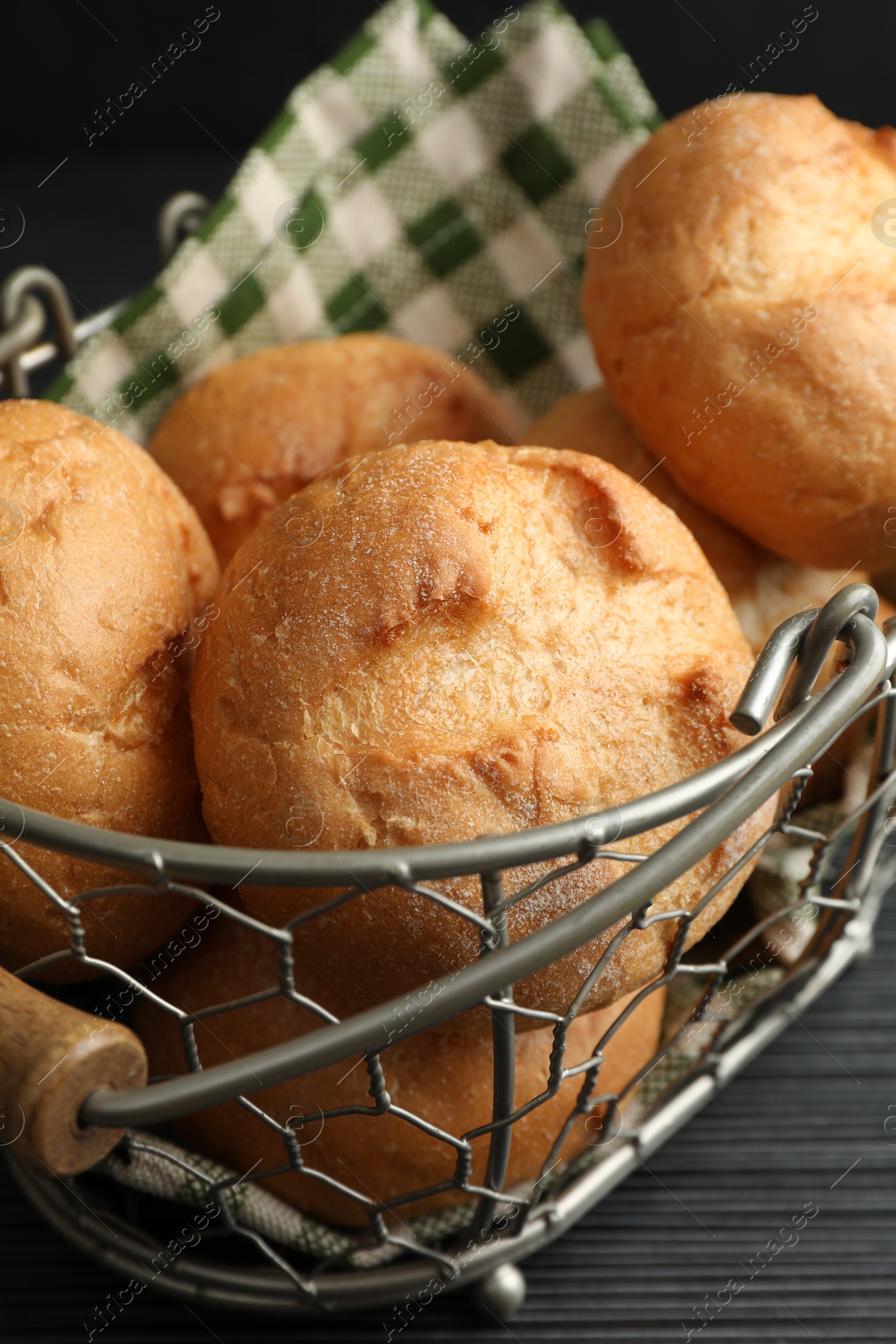 Photo of Metal basket with homemade tasty buns on black wooden table, closeup