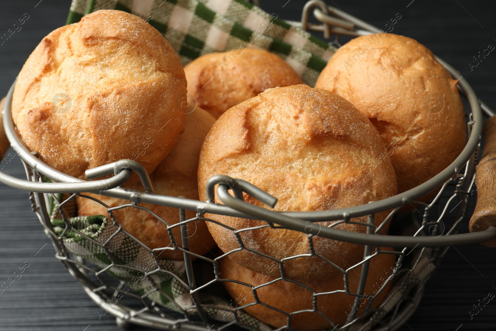 Photo of Metal basket with homemade tasty buns on black wooden table, closeup