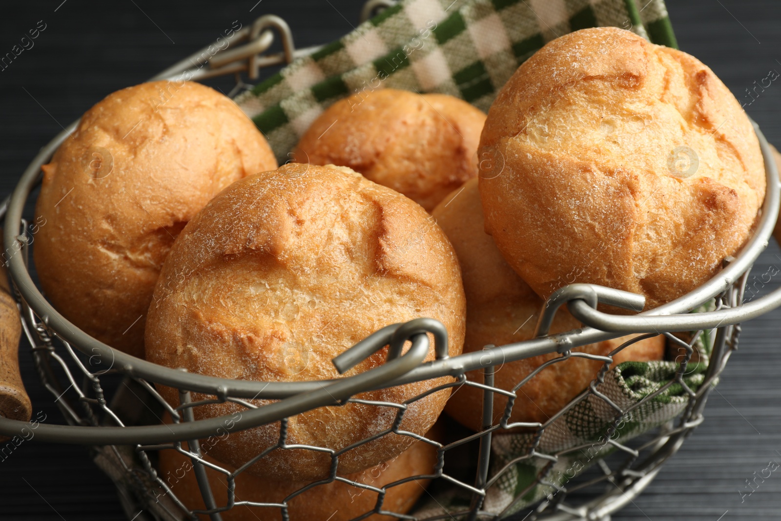 Photo of Metal basket with homemade tasty buns on black wooden table, closeup