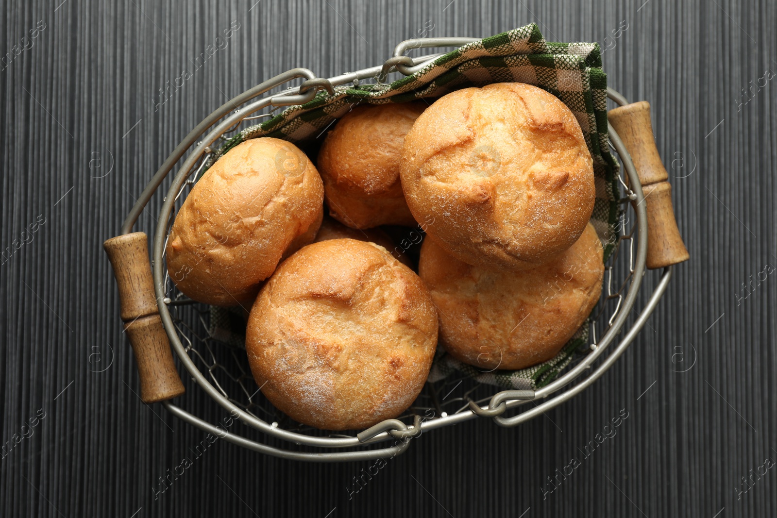 Photo of Metal basket with homemade tasty buns on black wooden table, top view