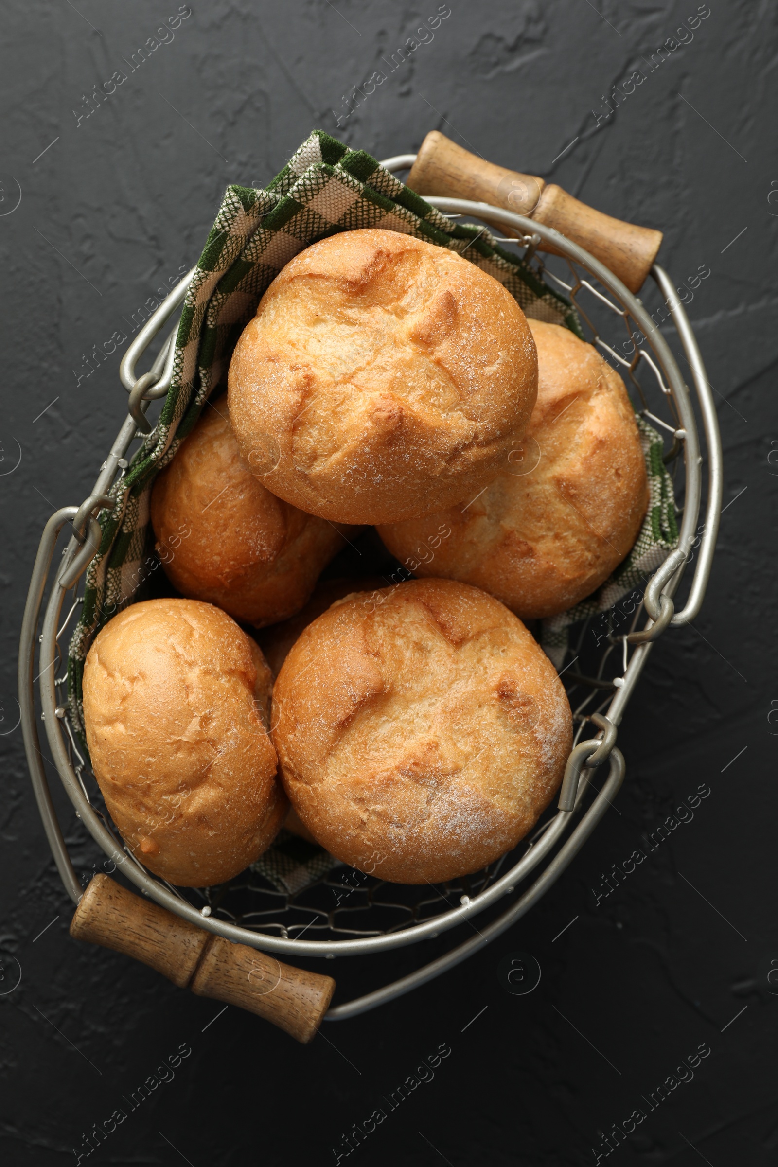 Photo of Metal basket with homemade tasty buns on black textured table, top view