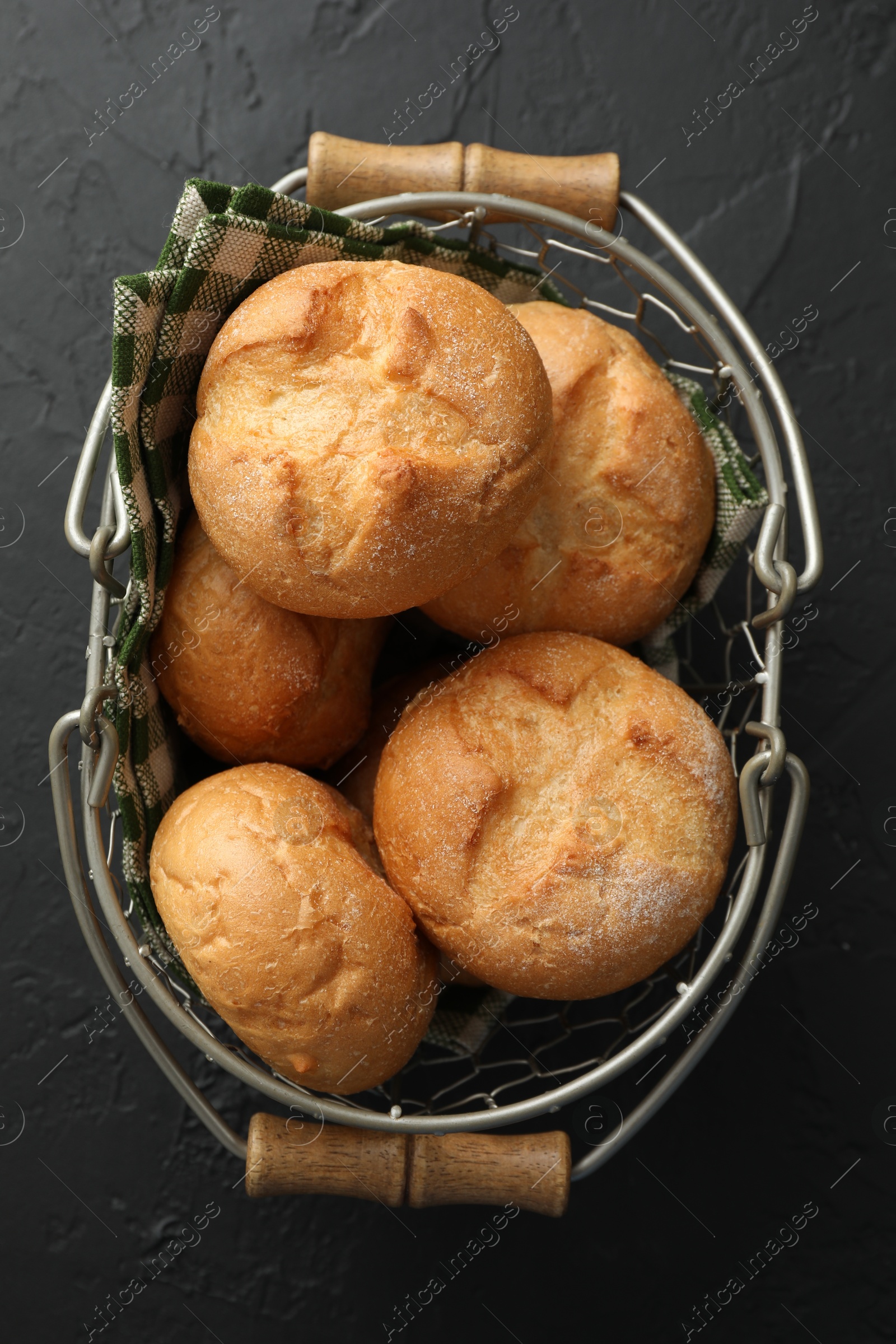 Photo of Metal basket with homemade tasty buns on black textured table, top view