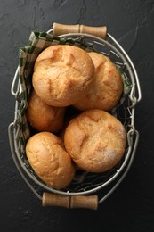 Metal basket with homemade tasty buns on black textured table, top view