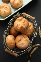 Photo of Homemade tasty buns and spikelets on black textured table, flat lay