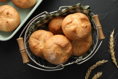 Photo of Homemade tasty buns and spikelets on black textured table, flat lay