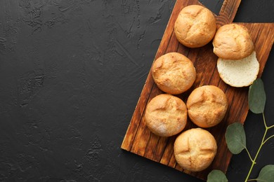 Photo of Homemade tasty buns and eucalyptus branch on black textured table, flat lay. Space for text