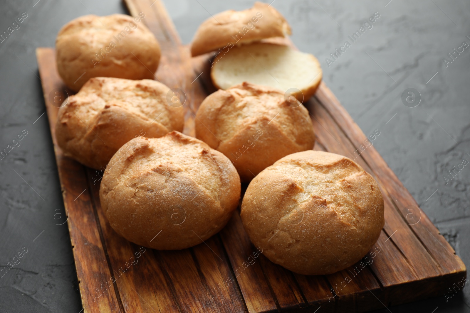 Photo of Board with homemade tasty buns on black textured table, closeup