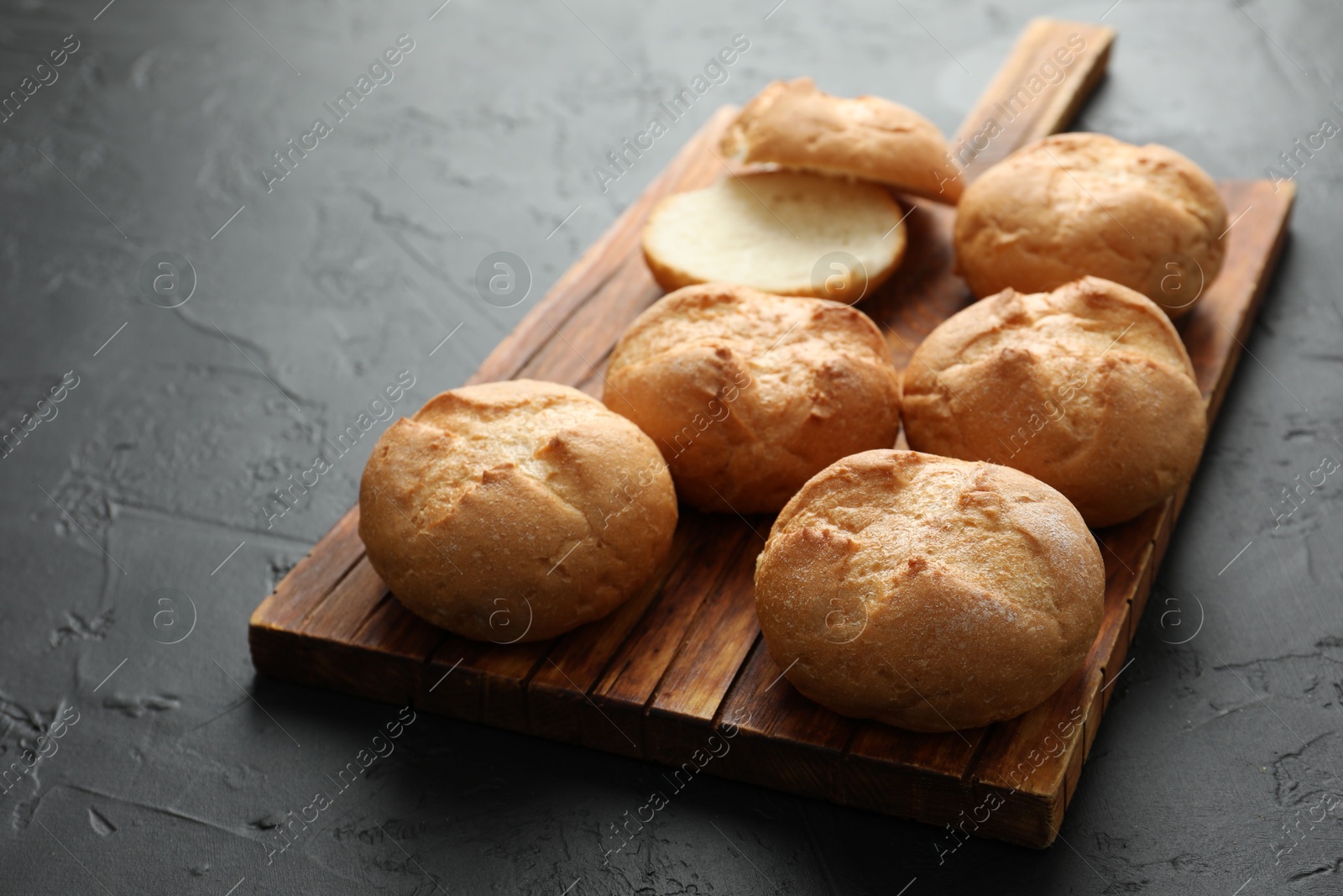 Photo of Board with homemade tasty buns on black textured table, closeup