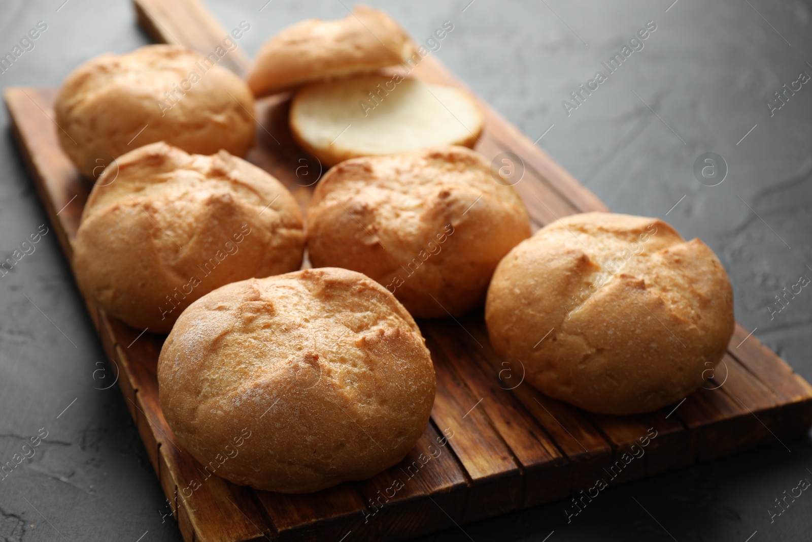 Photo of Board with homemade tasty buns on black textured table, closeup