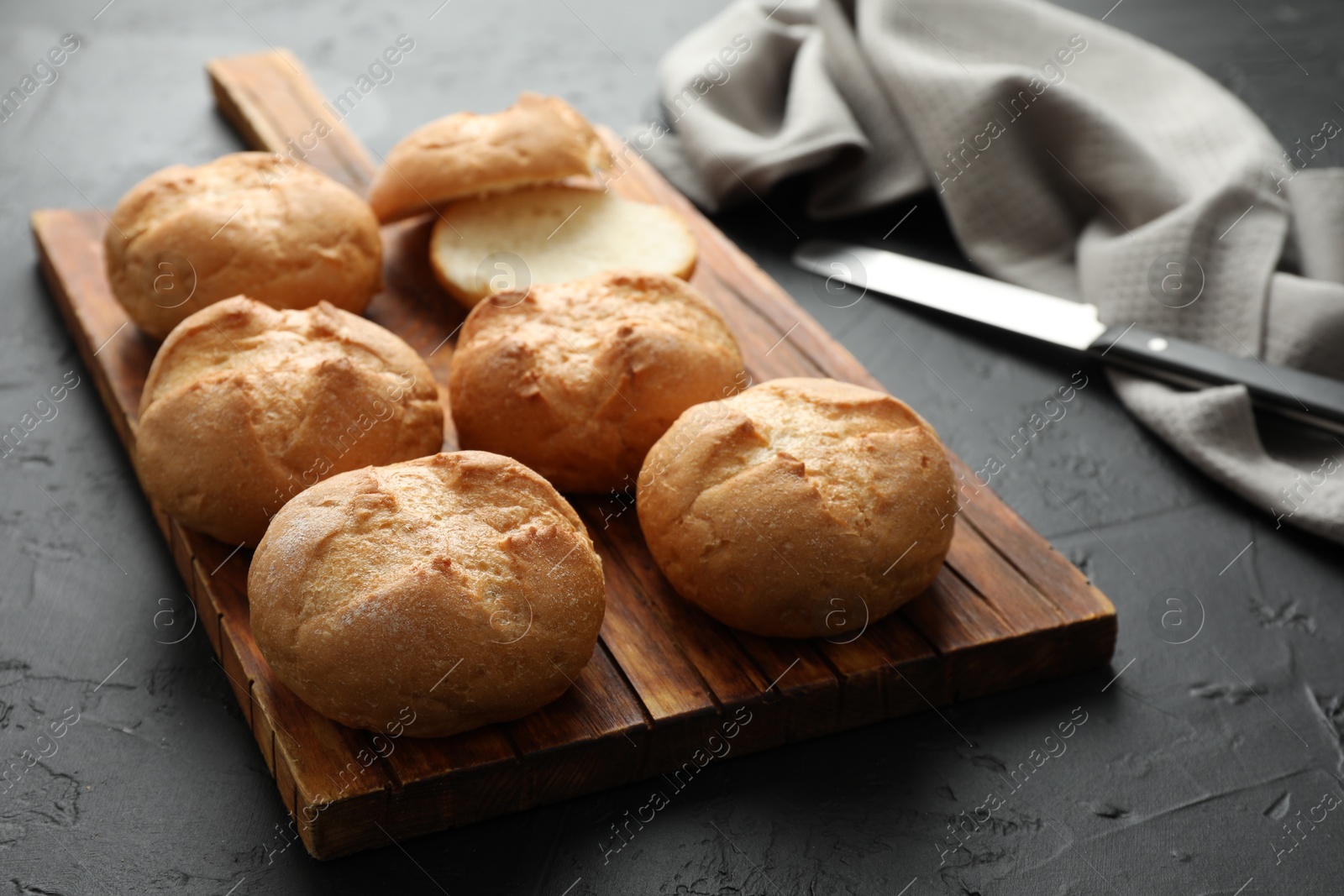 Photo of Board with homemade tasty buns on black textured table, closeup