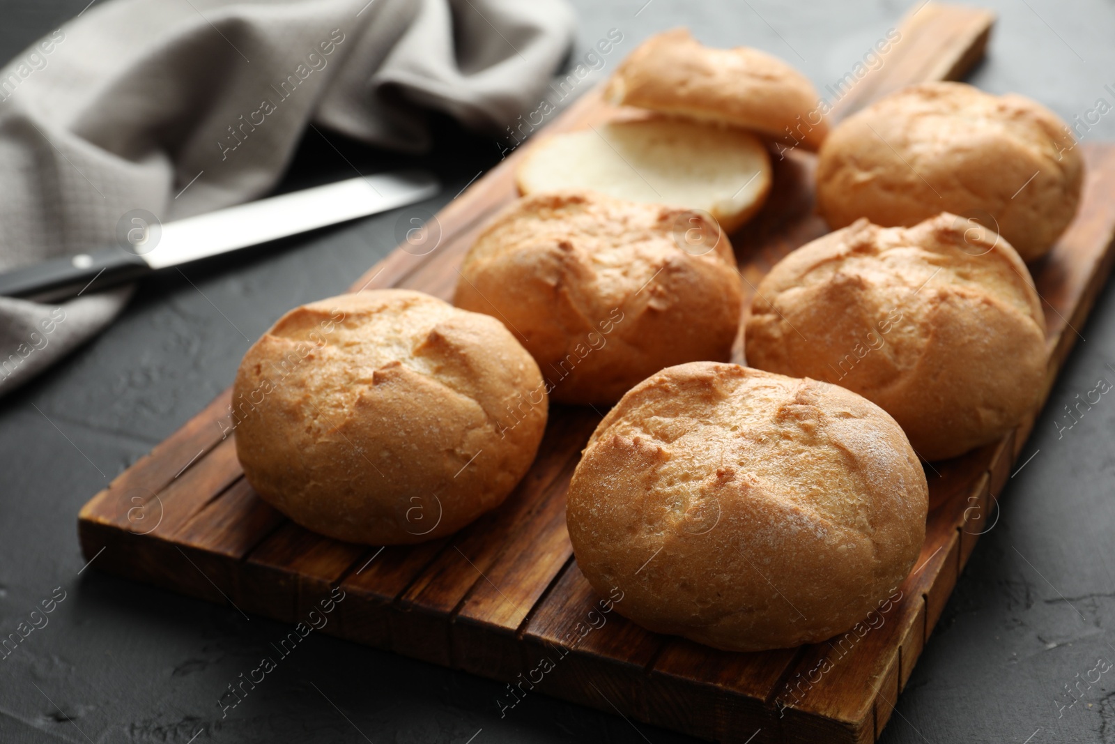 Photo of Board with homemade tasty buns on black textured table, closeup