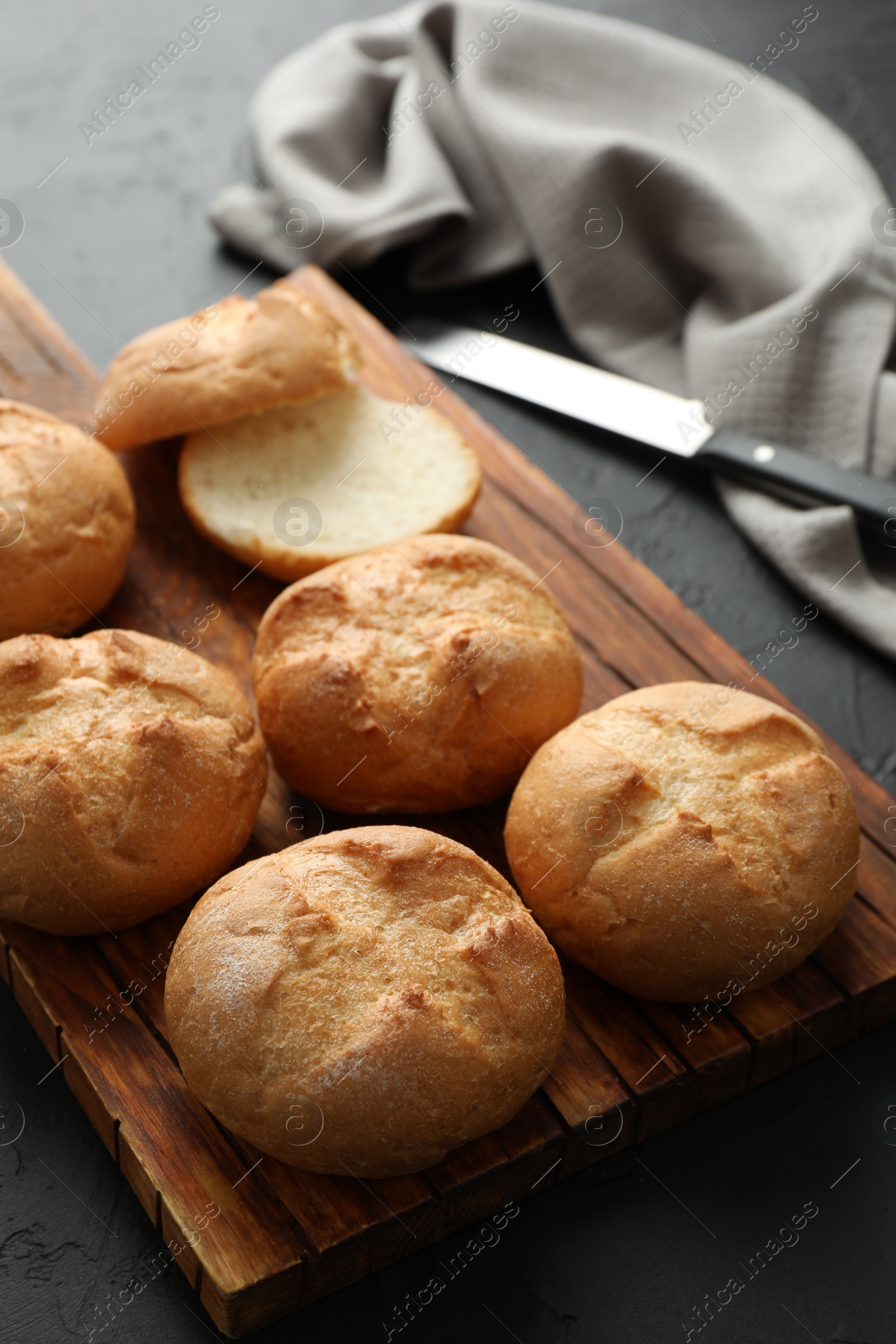 Photo of Board with homemade tasty buns on black textured table, closeup