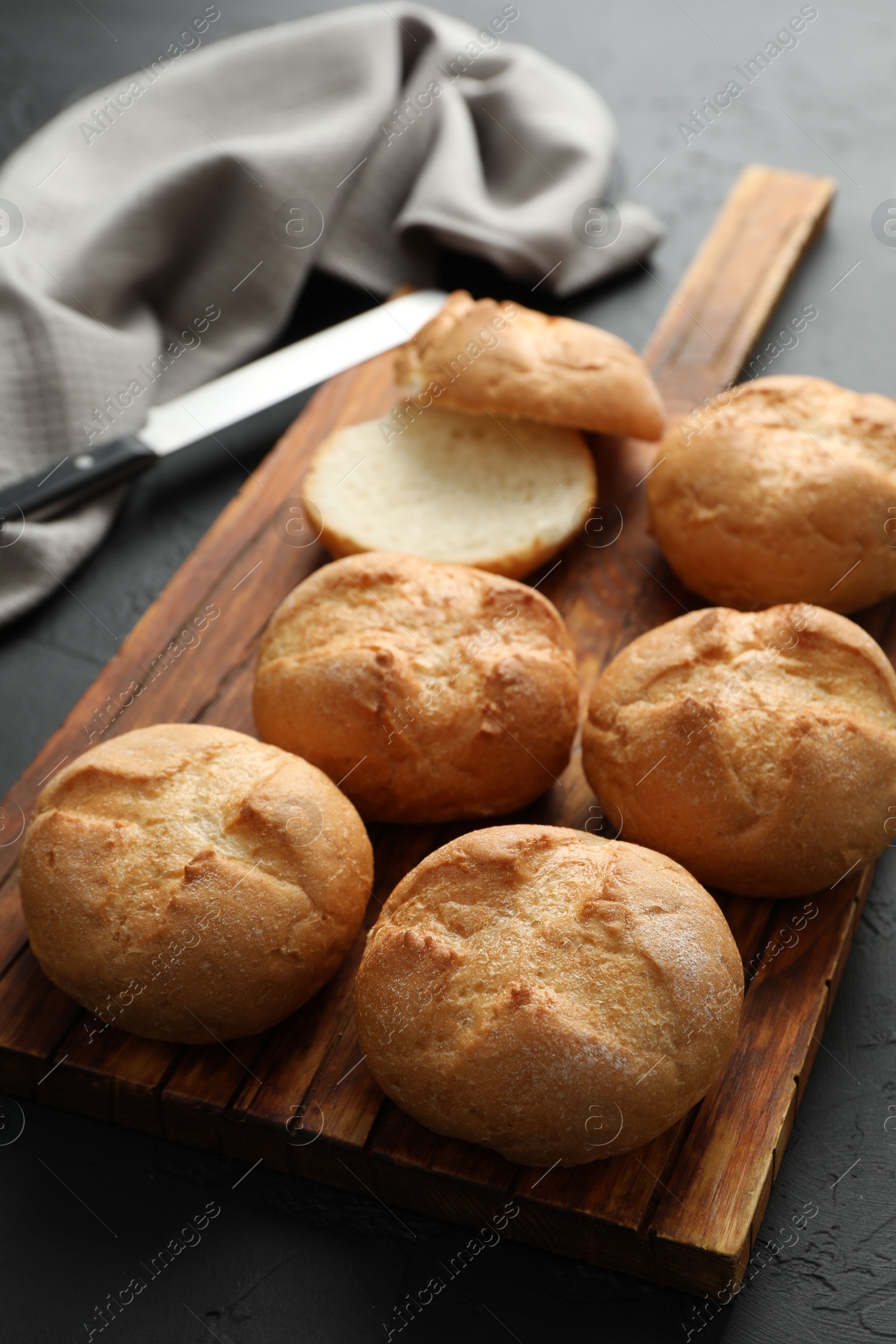 Photo of Board with homemade tasty buns on black textured table, closeup