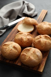 Photo of Board with homemade tasty buns on black textured table, closeup