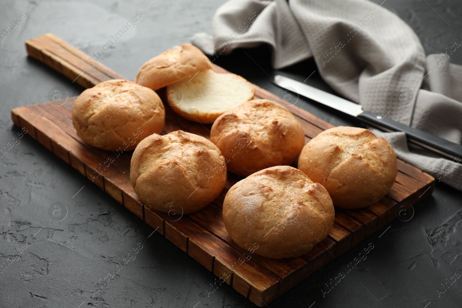 Photo of Board with homemade tasty buns on black textured table, closeup