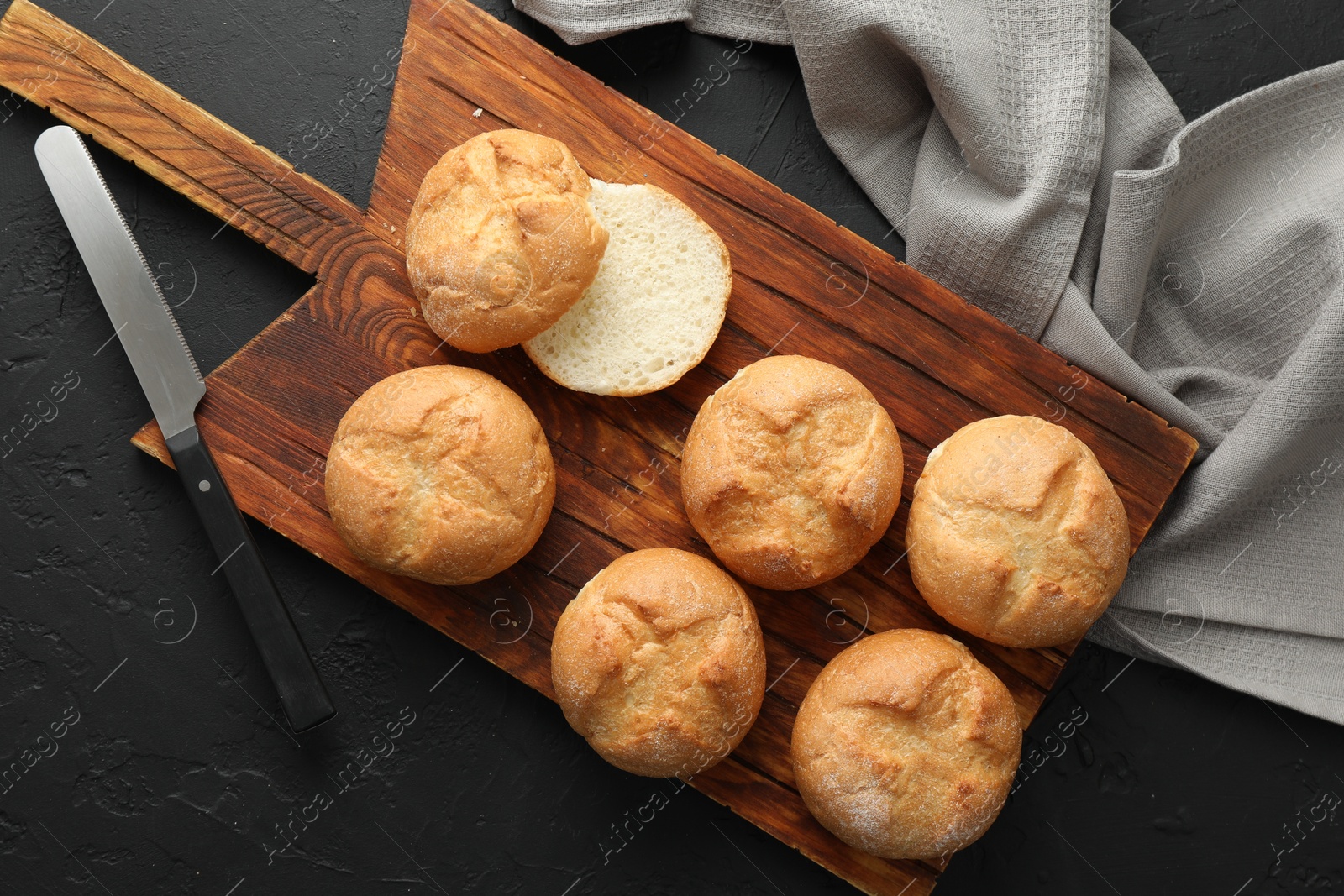 Photo of Board with homemade tasty buns and knife on black textured table, flat lay