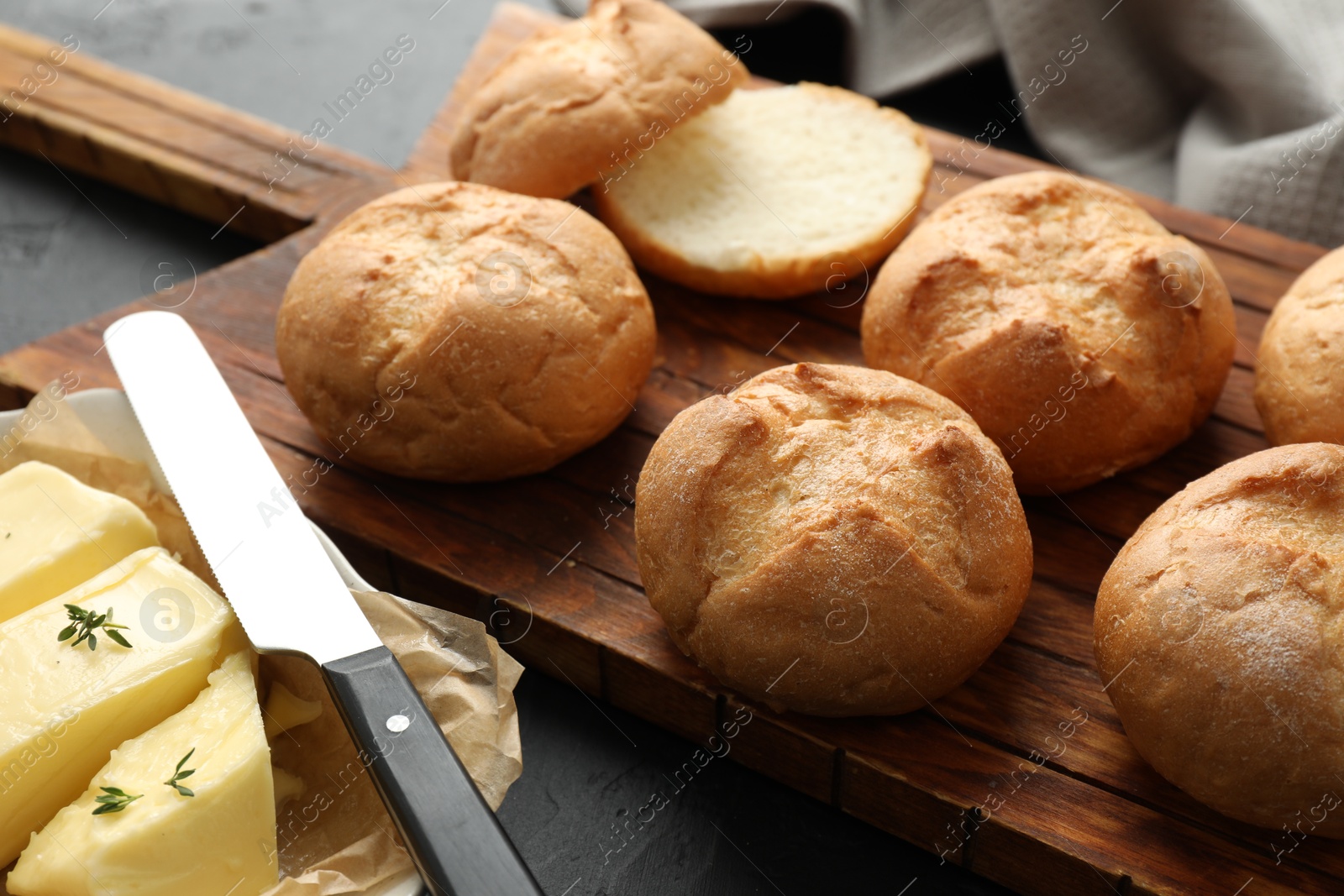 Photo of Board with homemade tasty buns, butter and knife on black table, closeup