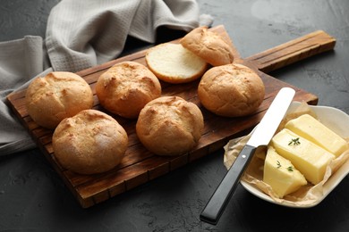 Photo of Board with homemade tasty buns, butter and knife on black textured table, closeup