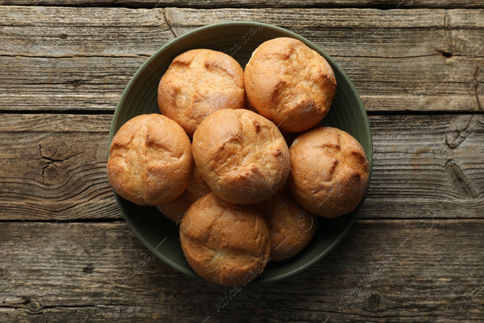 Photo of Homemade tasty buns in bowl on wooden table, top view