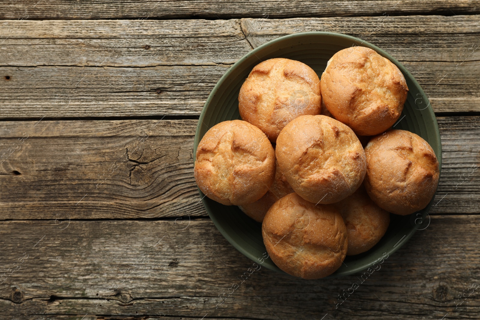 Photo of Homemade tasty buns in bowl on wooden table, top view. Space for text