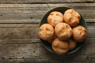 Photo of Homemade tasty buns in bowl on wooden table, top view. Space for text