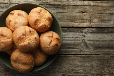 Photo of Homemade tasty buns in bowl on wooden table, top view. Space for text