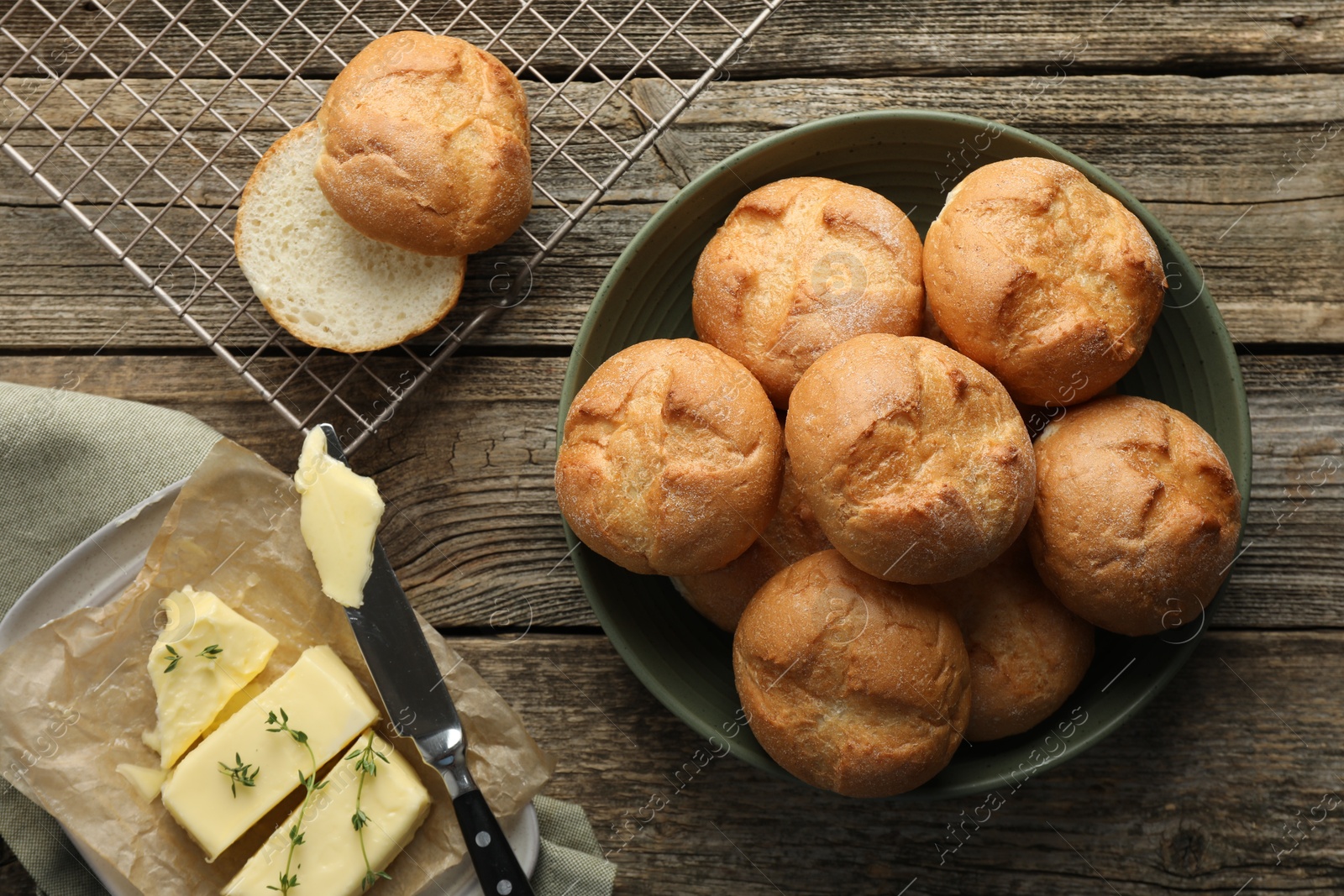 Photo of Homemade tasty buns, butter and knife on wooden table, flat lay