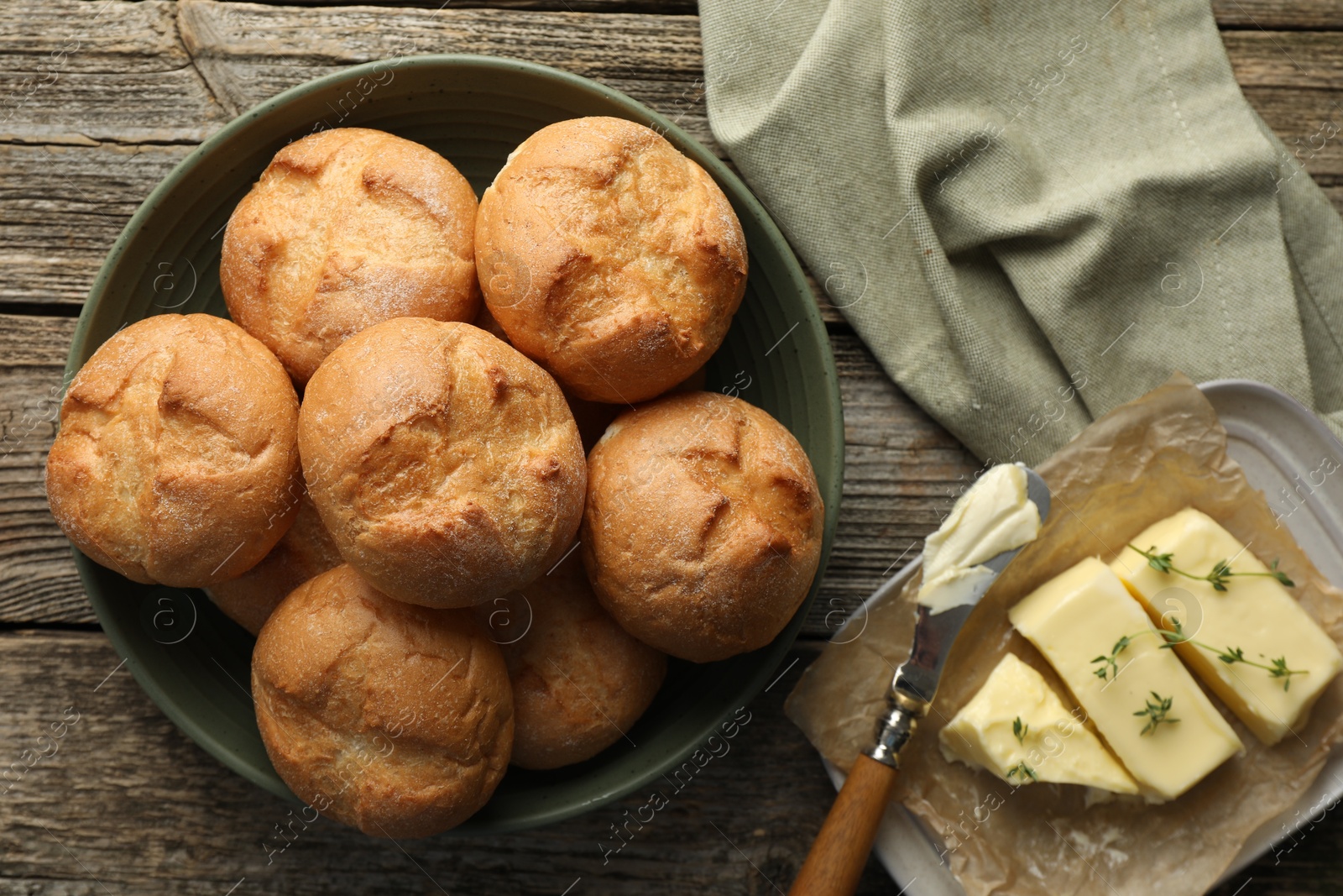 Photo of Homemade tasty buns, butter and knife on wooden table, flat lay