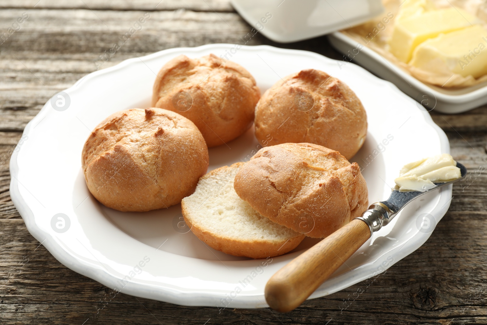 Photo of Plate with homemade tasty buns, butter and knife on wooden table, closeup