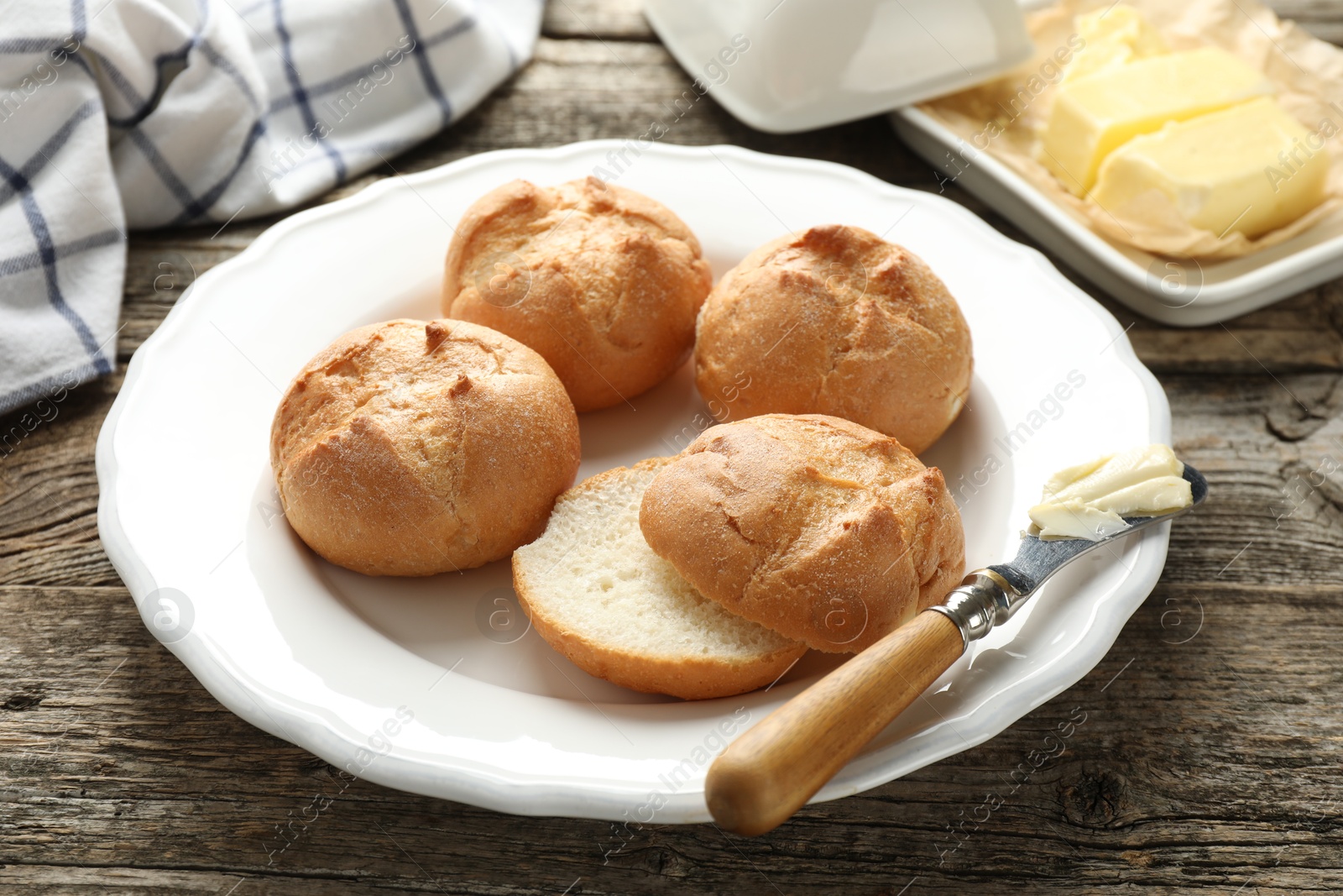 Photo of Plate with homemade tasty buns, butter and knife on wooden table, closeup