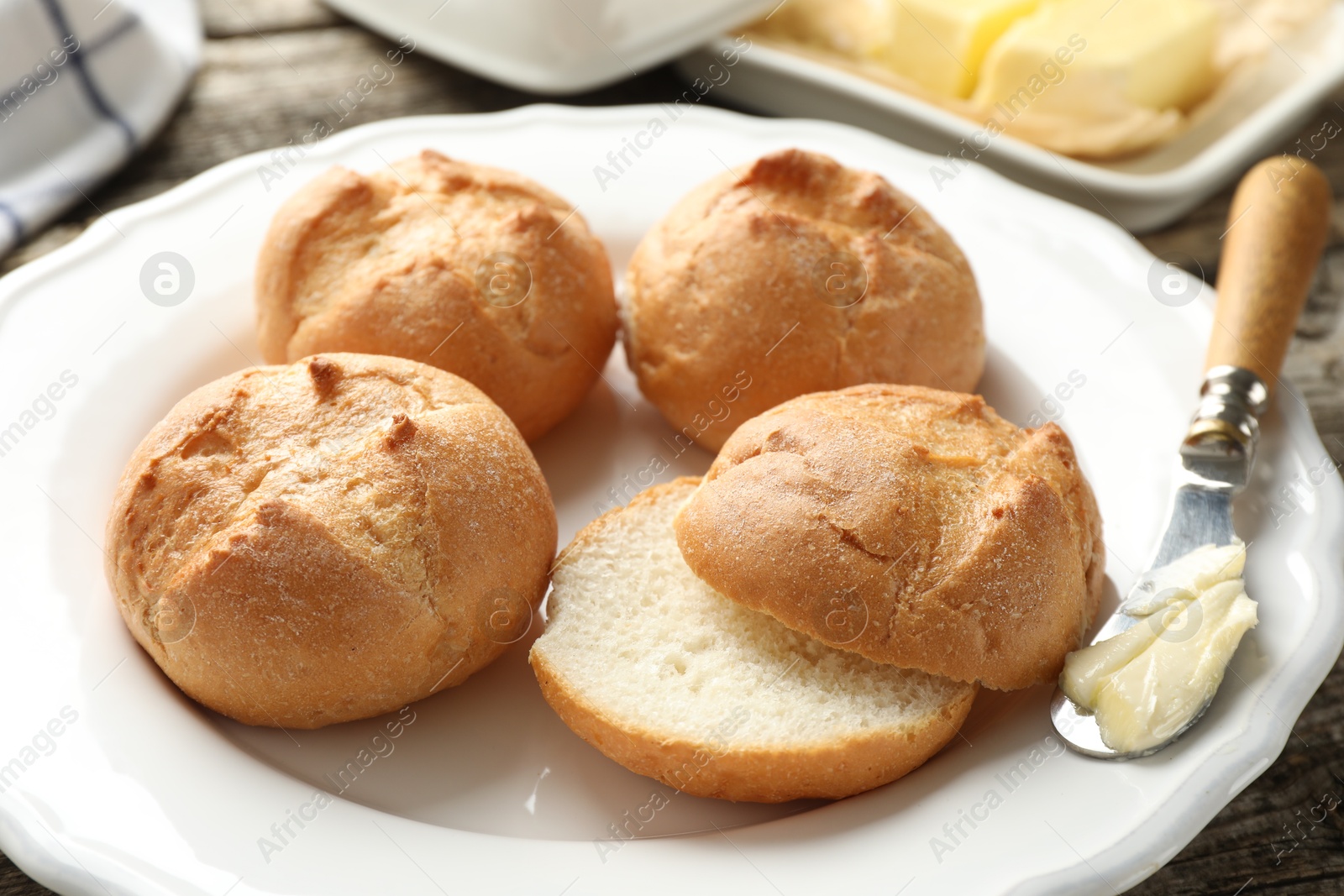 Photo of Plate with homemade tasty buns, butter and knife on table, closeup