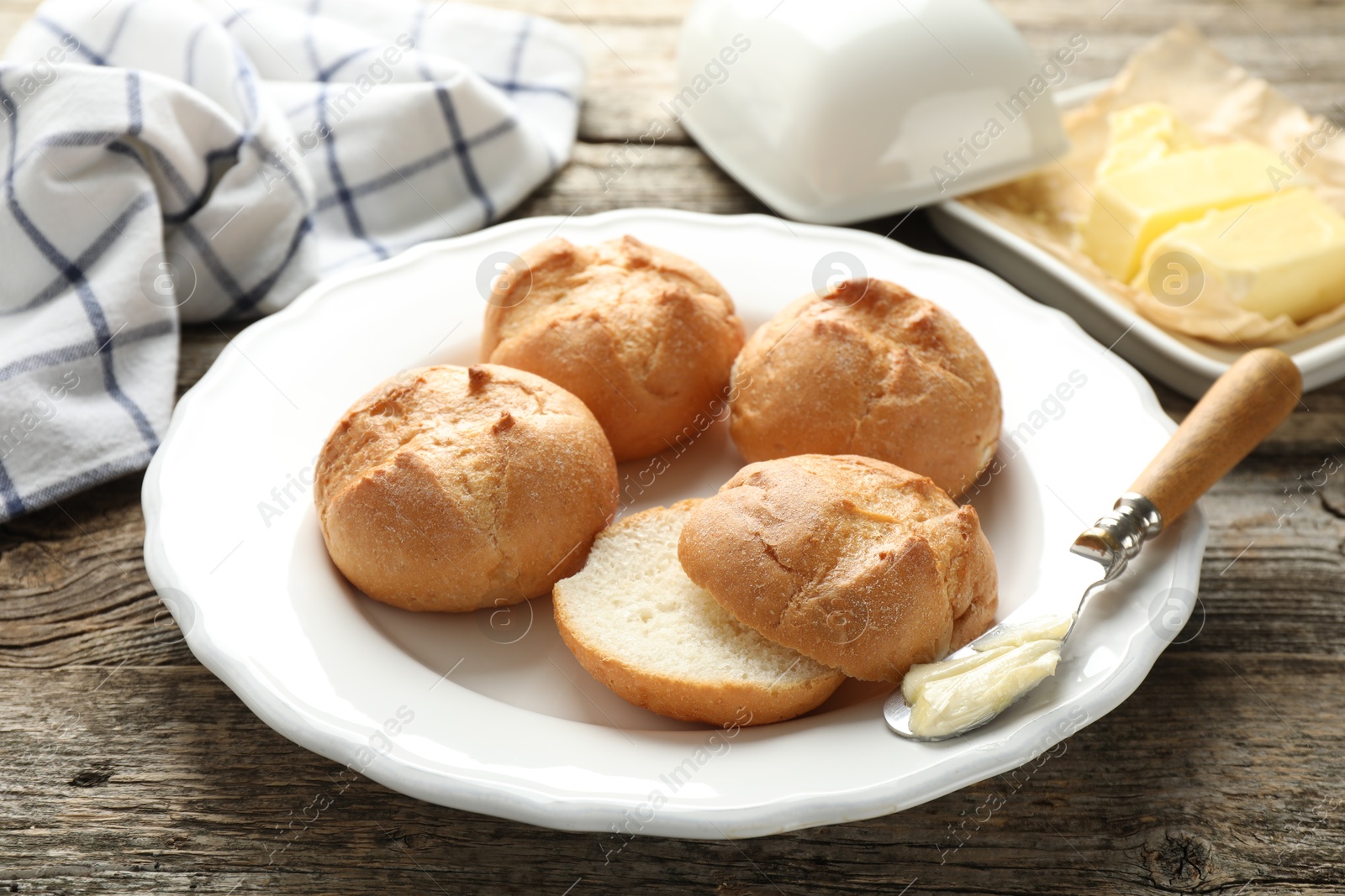 Photo of Plate with homemade tasty buns, butter and knife on wooden table, closeup