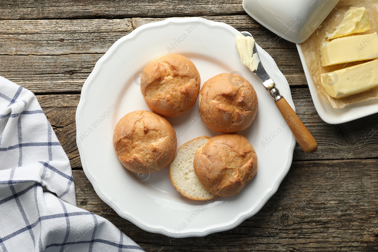 Photo of Plate with homemade tasty buns, butter and knife on wooden table, flat lay