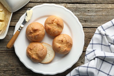 Photo of Plate with homemade tasty buns, butter and knife on wooden table, flat lay