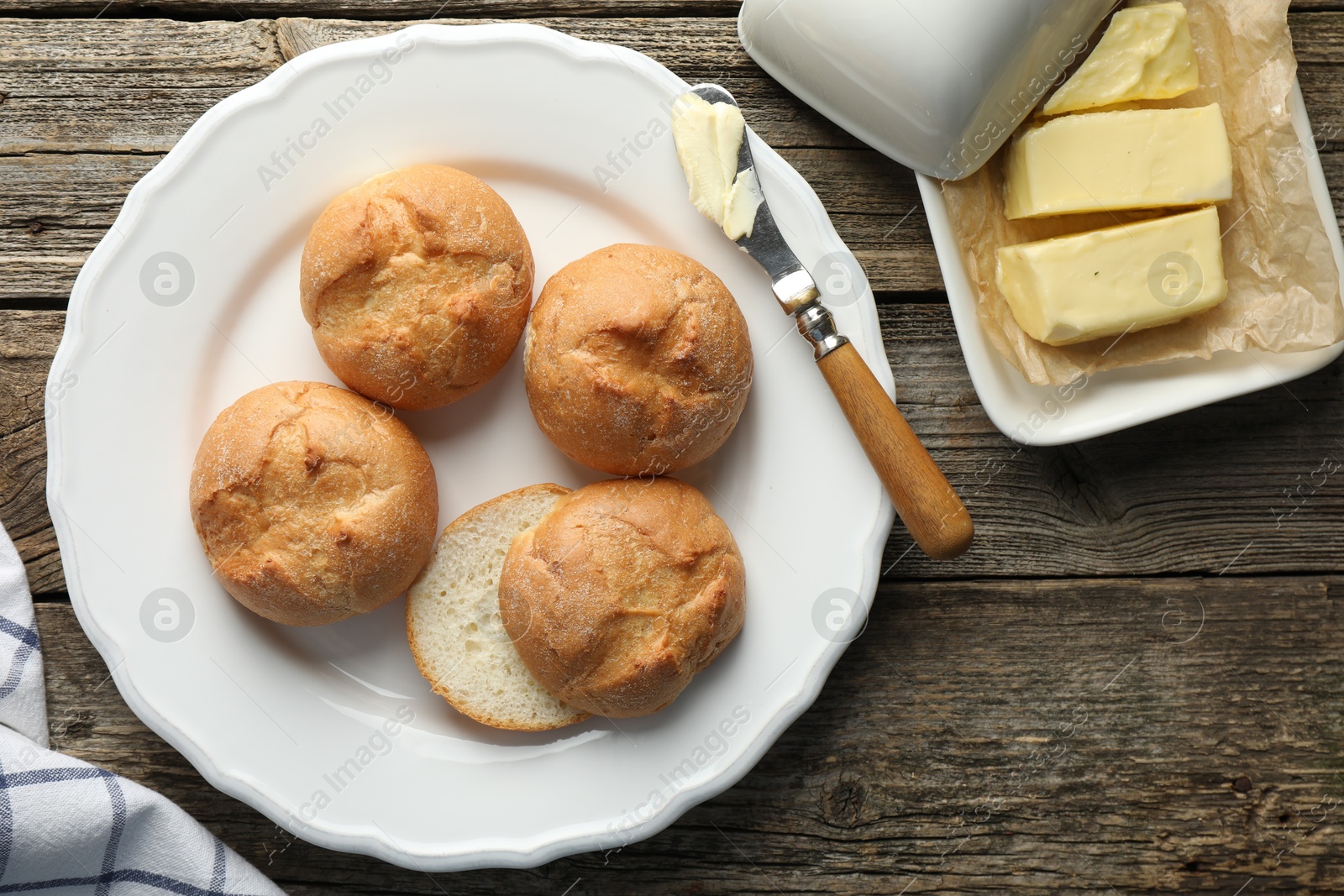 Photo of Plate with homemade tasty buns, butter and knife on wooden table, flat lay