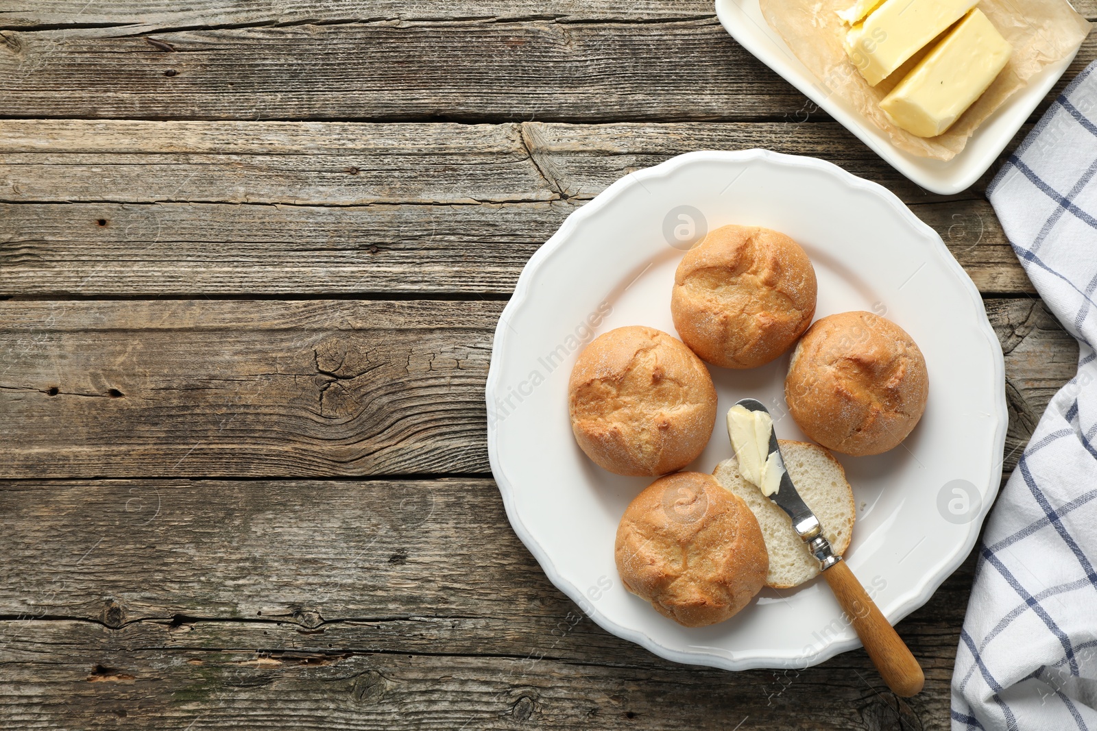 Photo of Plate with homemade tasty buns, butter and knife on wooden table, flat lay. Space for text