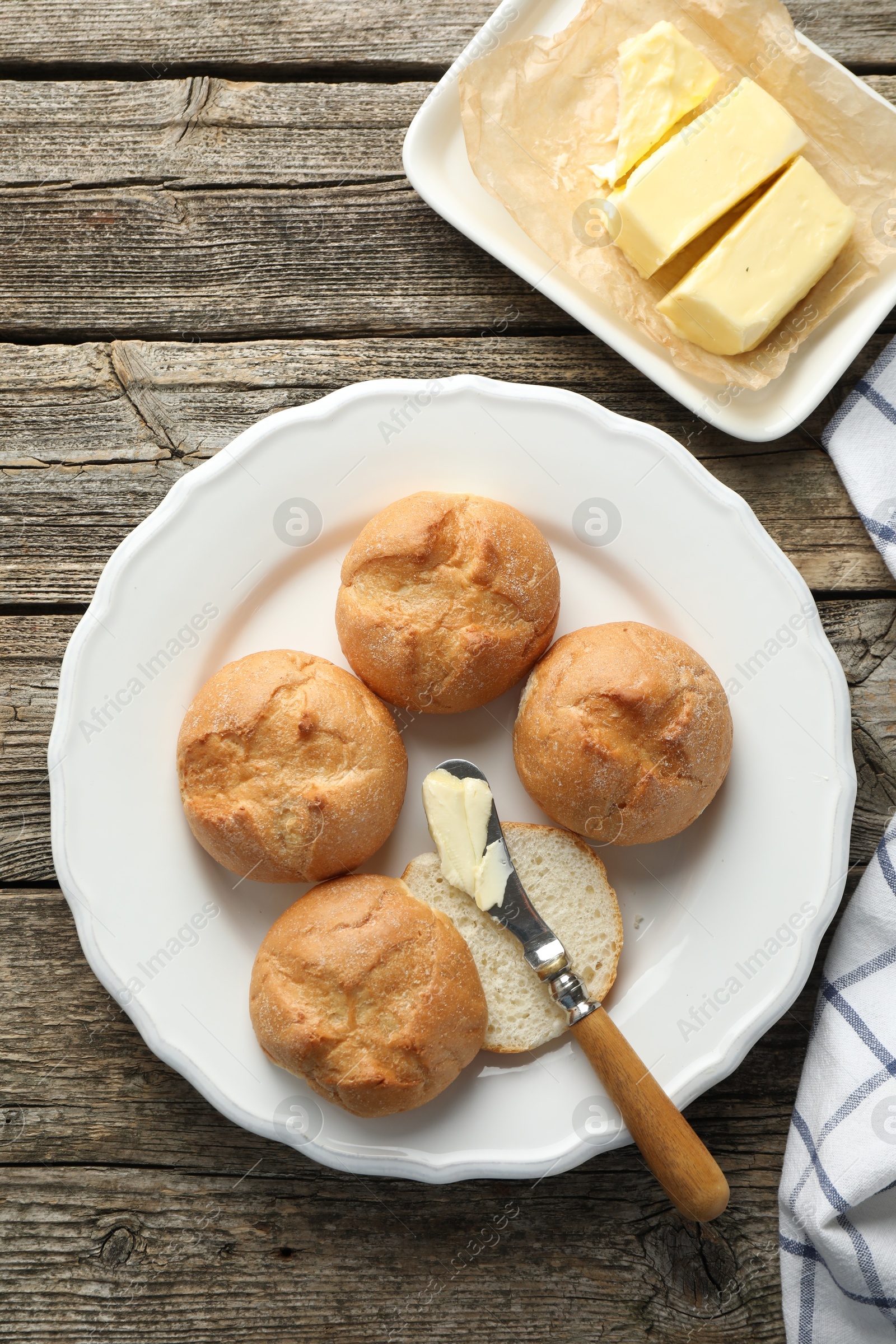 Photo of Plate with homemade tasty buns, butter and knife on wooden table, flat lay