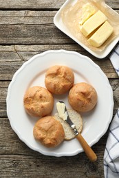 Plate with homemade tasty buns, butter and knife on wooden table, flat lay