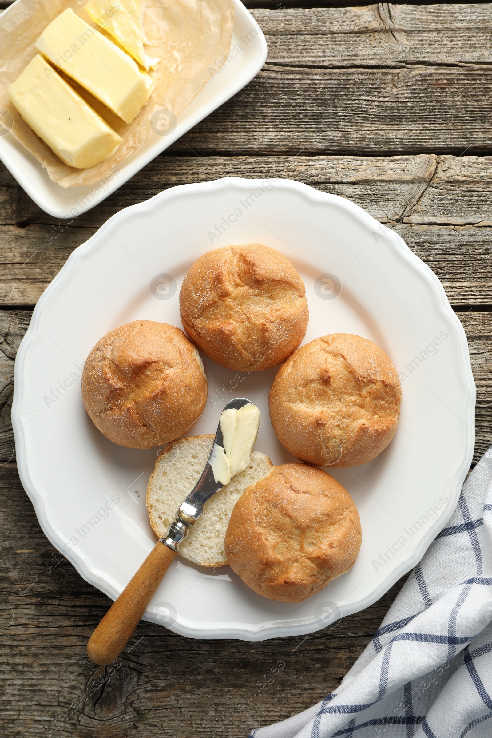 Photo of Plate with homemade tasty buns, butter and knife on wooden table, flat lay