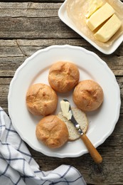 Photo of Plate with homemade tasty buns, butter and knife on wooden table, flat lay