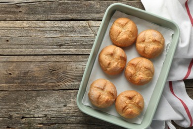 Photo of Homemade tasty buns in baking dish on wooden table, top view. Space for text