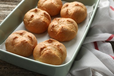 Photo of Homemade tasty buns in baking dish on wooden table, closeup