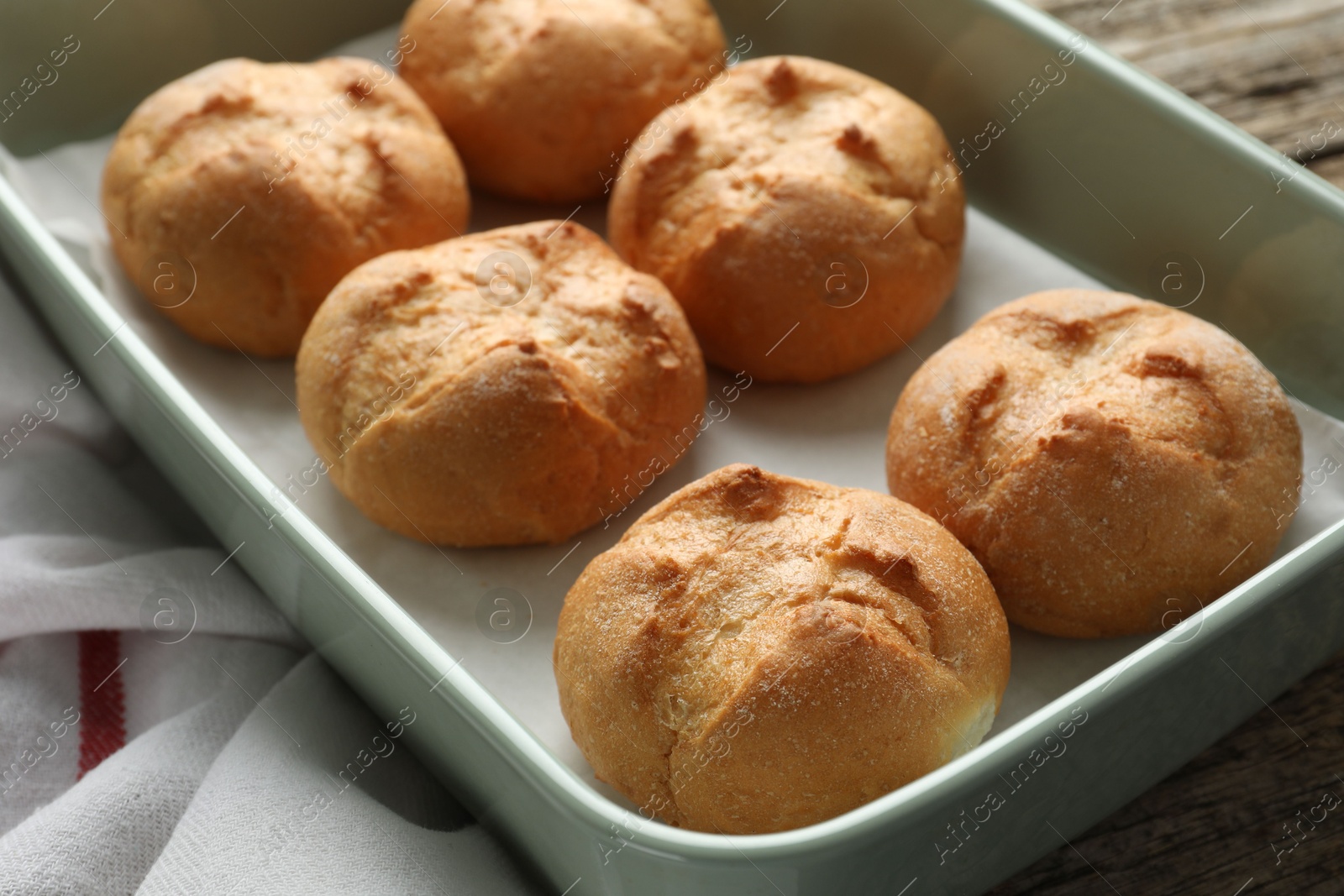 Photo of Homemade tasty buns in baking dish on wooden table, closeup