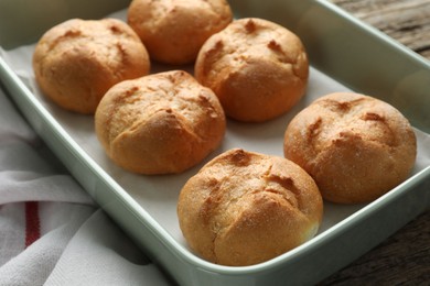 Photo of Homemade tasty buns in baking dish on wooden table, closeup