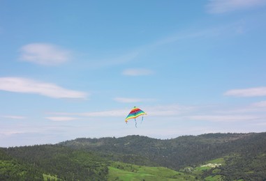 One colorful kite flying in mountains under blue sky